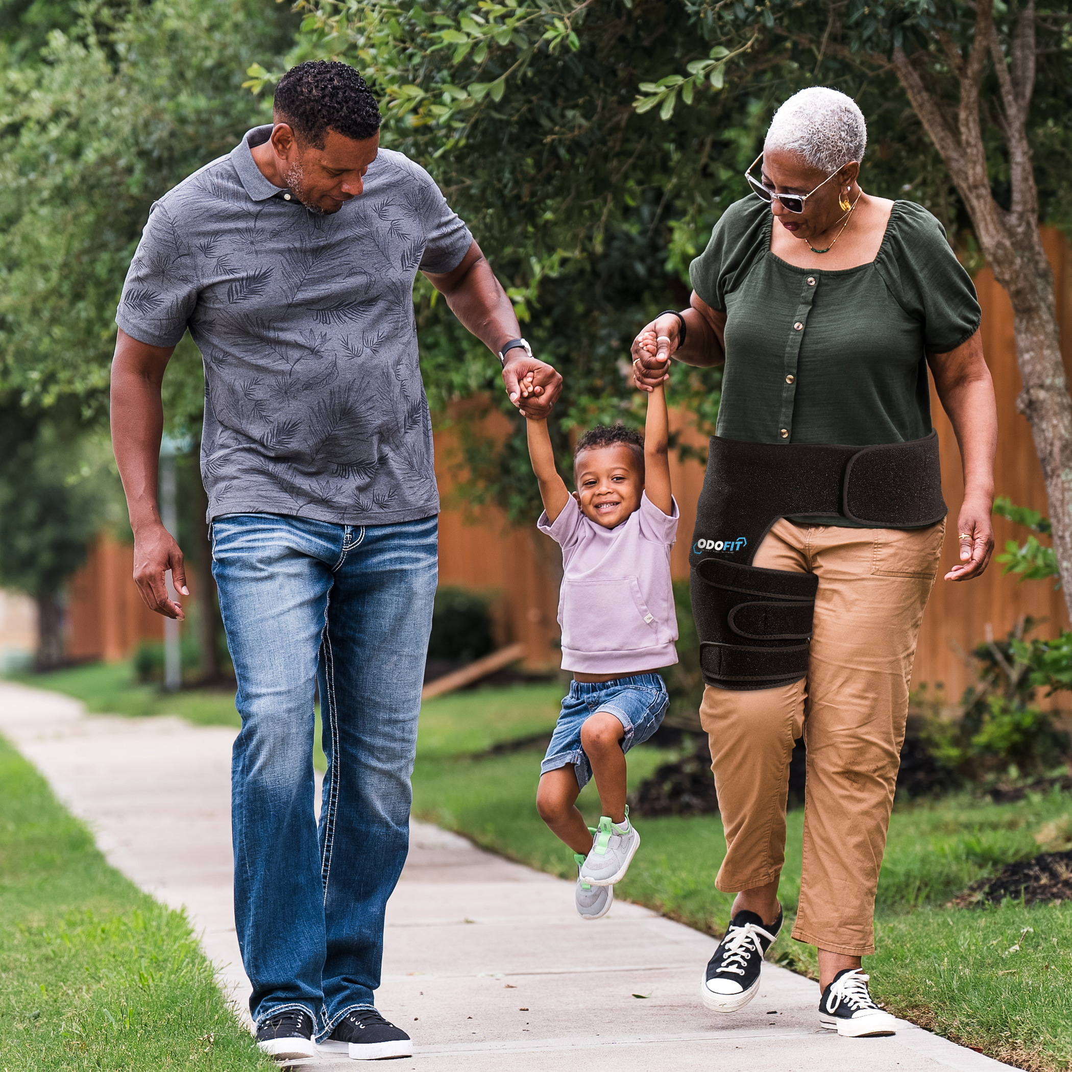 Grandparents wearing the ODOFIT hip brace walking outdoors while swinging their grandson between them
